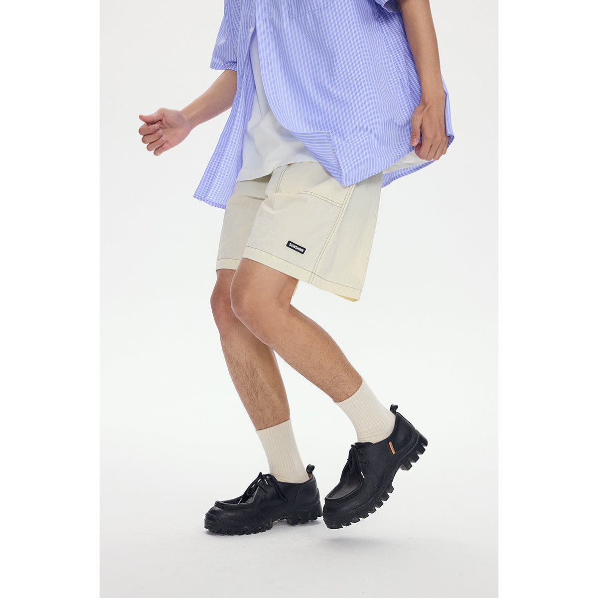 Cropped view of a model wearing cream shorts with a large patch pocket and contrast stitching.
