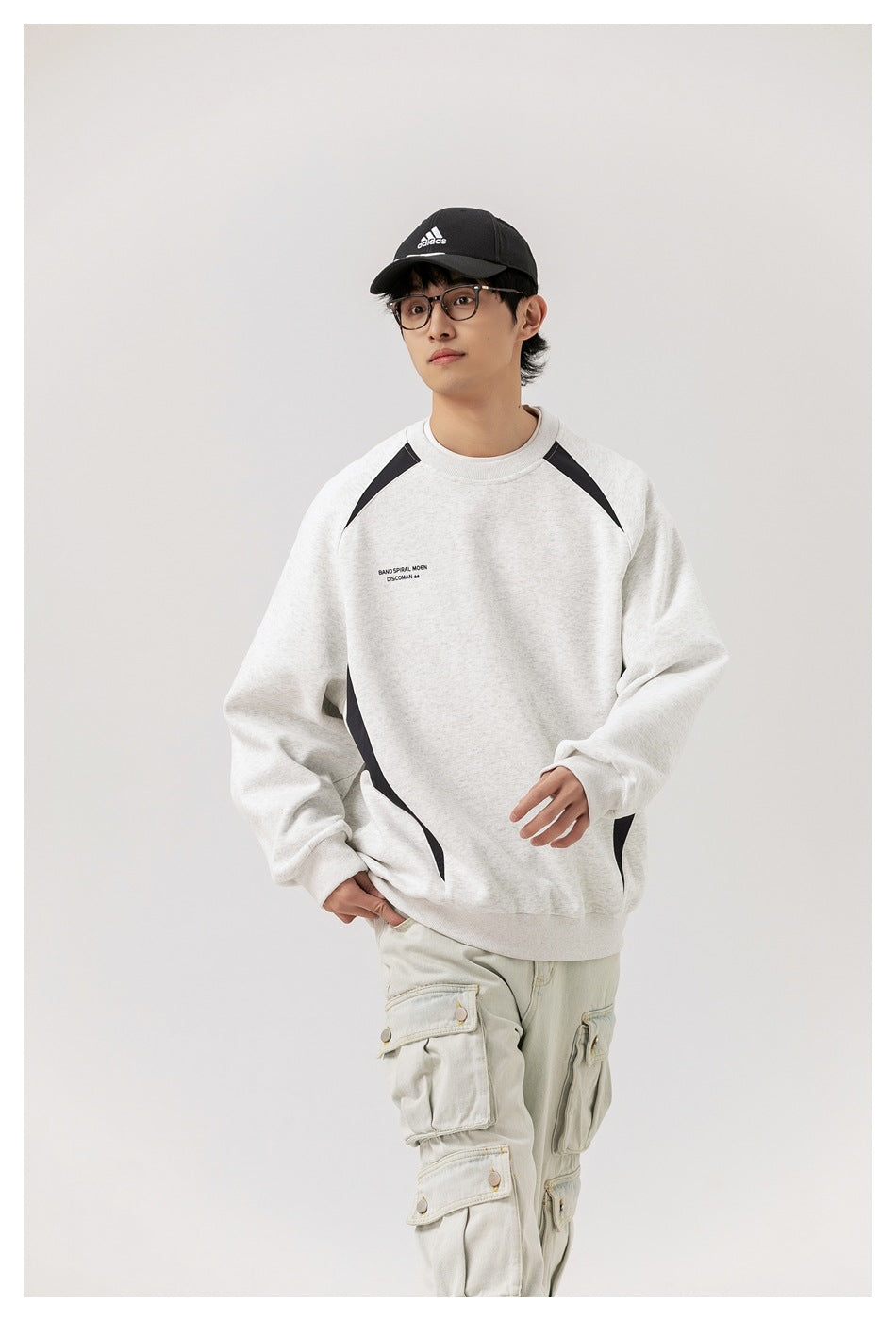 Model wearing an oversized light gray sweatshirt with black curved panels and small chest text.