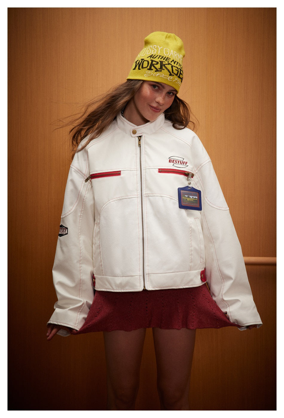 Model wearing a white zip-front jacket with red pocket zippers and a burgundy skirt, facing forward.