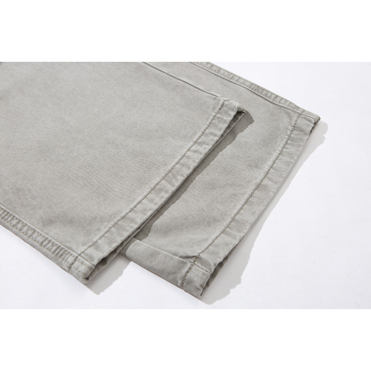 Close-up of the stitched hems on light gray pants, shown folded over each other.