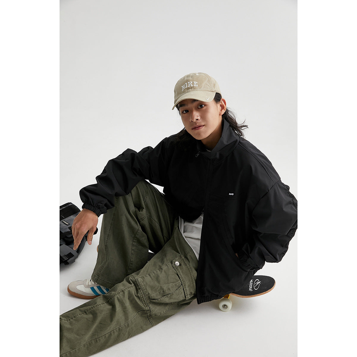 Seated model wearing a black zip-up jacket with a high collar and elastic cuffs and hem.