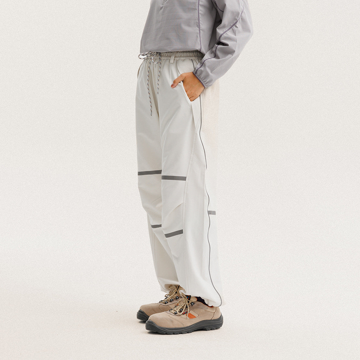 Side view of a model wearing loose ivory drawstring pants with dark gray bands and ankle cuffs.