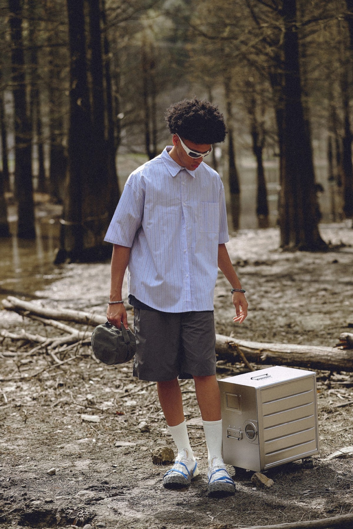 Full-length model wearing an oversized pale blue pinstriped short-sleeve button-up shirt with dark shorts.