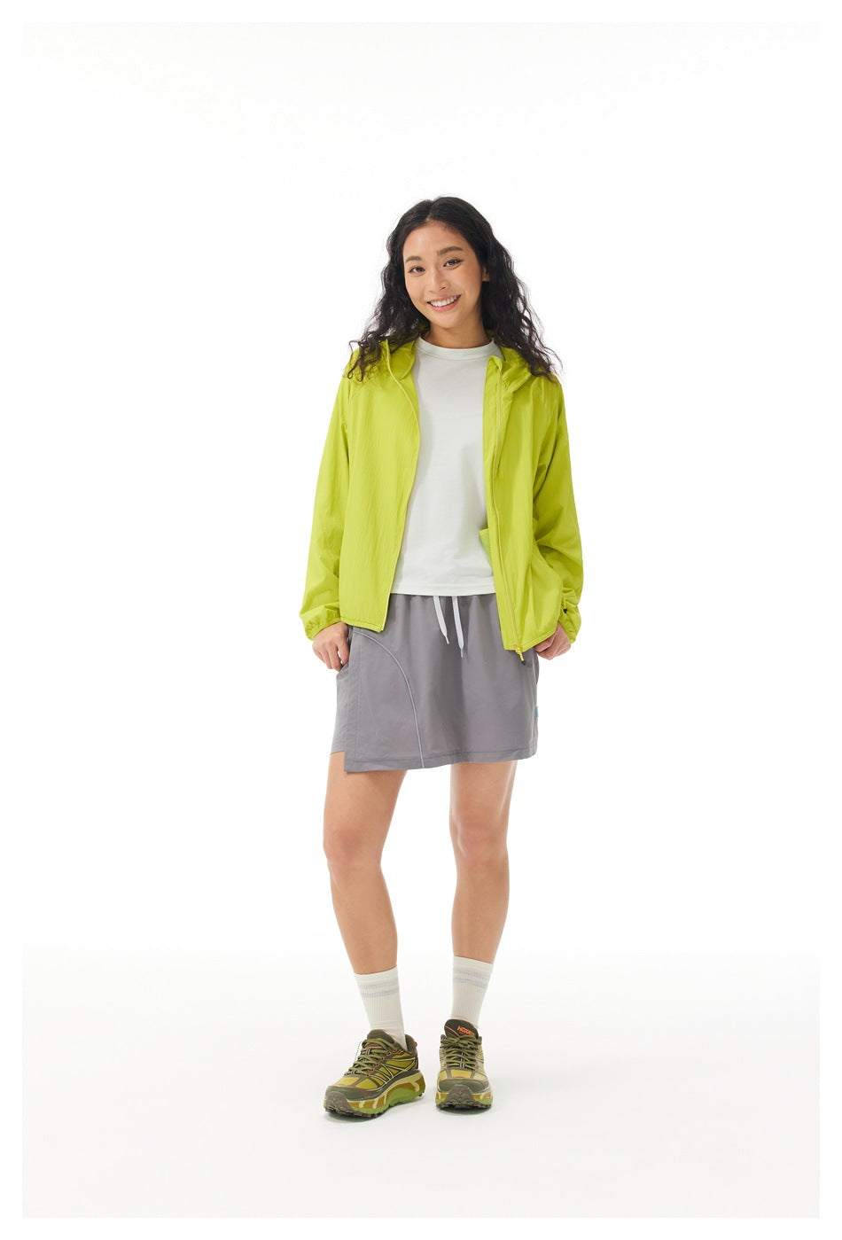 Model wearing an open lime hooded jacket over a white shirt with a gray skirt.