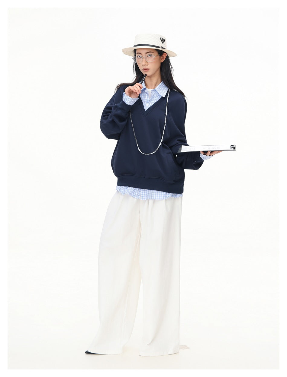 Full-length model wearing a navy V-neck sweatshirt over a blue checked shirt and wide white trousers.
