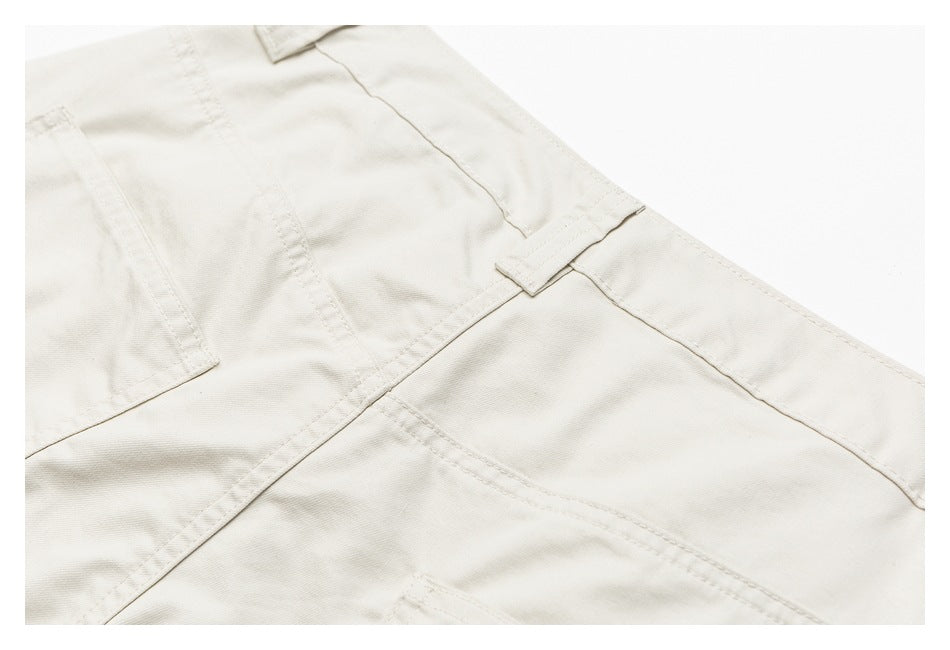 Close-up of ivory trousers showing a belt loop, waistband seam and pocket stitching.
