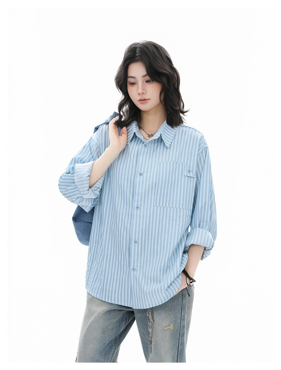 Model wearing a light blue striped button-up shirt with rolled sleeves, jeans and a denim bag over the shoulder