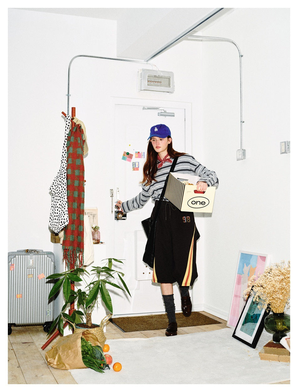 Model wearing a gray striped long-sleeve shirt and black shorts with red and yellow side stripes, carrying a box.
