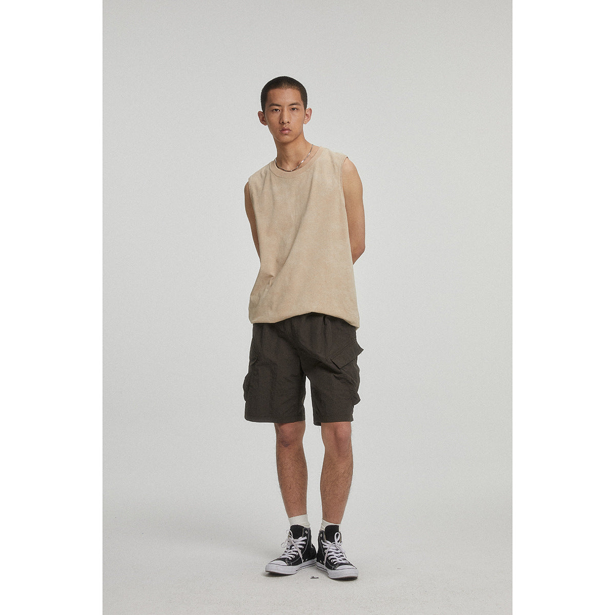 Full-length front view of a man wearing a beige sleeveless top and dark cargo shorts.
