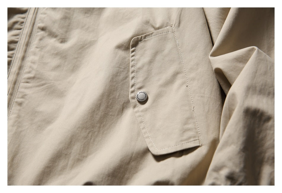 Close-up of a beige jacket pocket with a small round button and visible stitching.