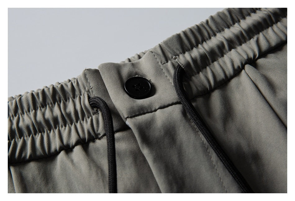 Close-up of gray shorts with a gathered elastic waistband, black button, and black drawcords.
