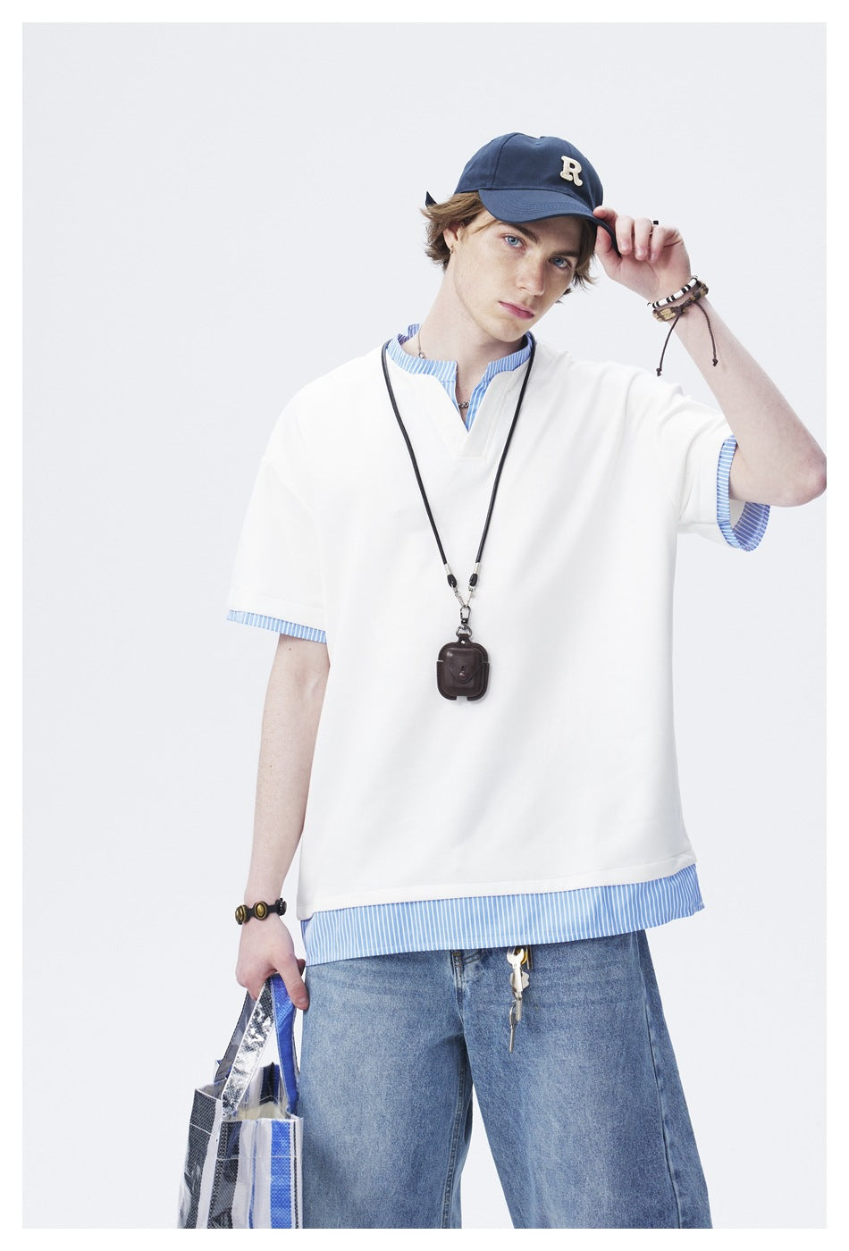 Model wearing an oversized white V-neck tee over a blue-and-white striped shirt and wide-leg jeans.