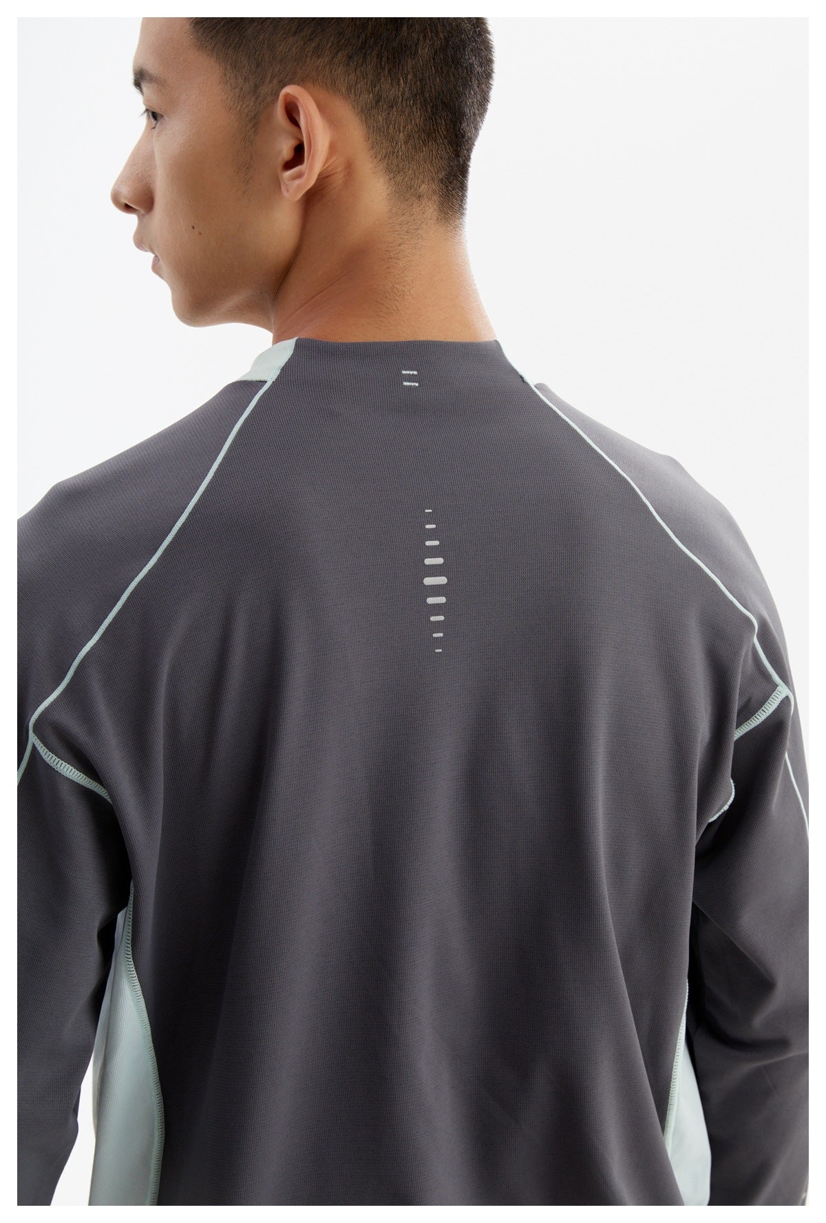 Back view of a model wearing a charcoal long-sleeve top with pale aqua side panels and reflective dash details.