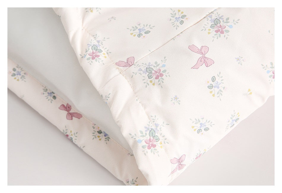 Close-up of a folded edge on pale ivory fabric with pastel floral clusters and pink bow prints.