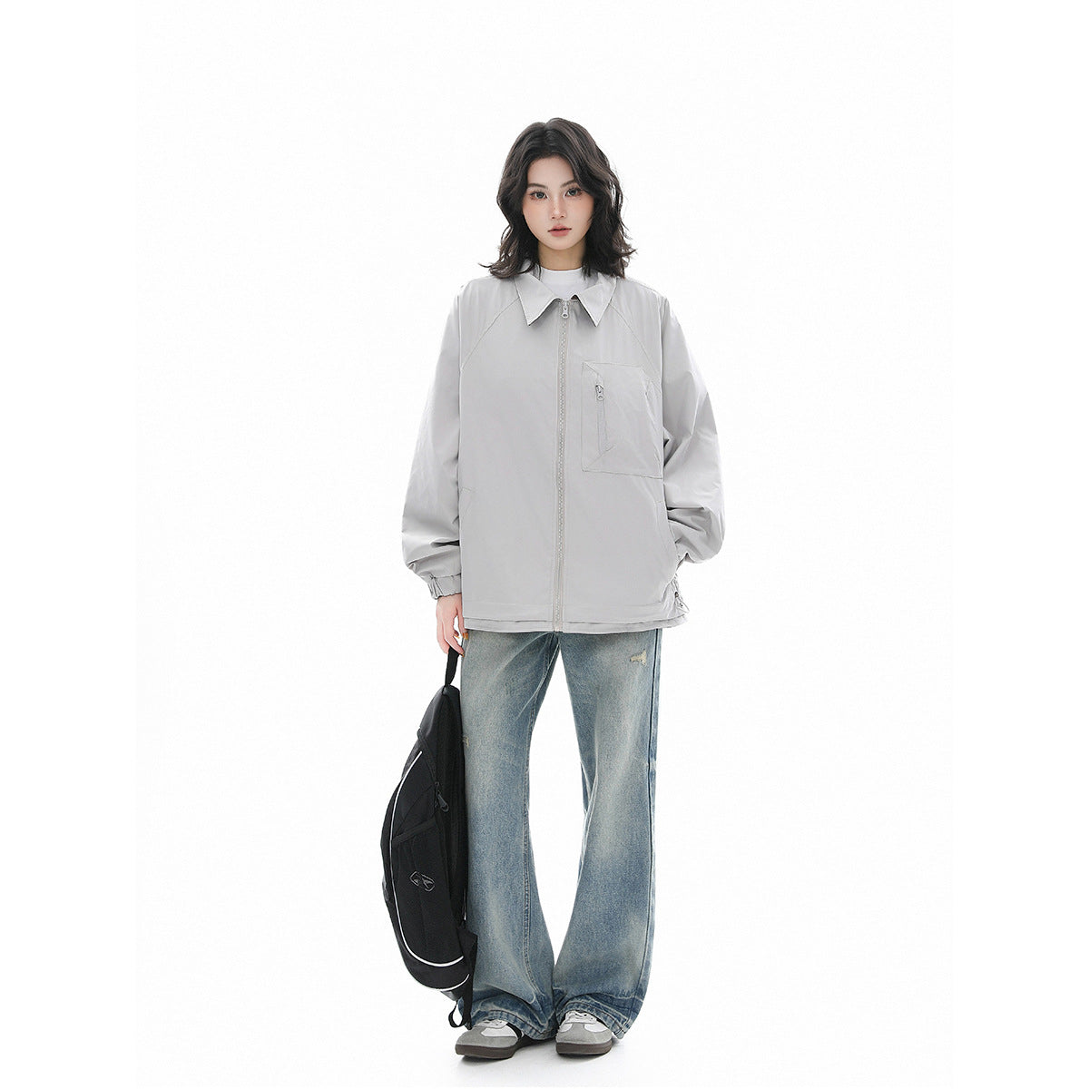 Full-length model wearing a light gray zip-front jacket with a pointed collar and chest pocket, paired with jeans.