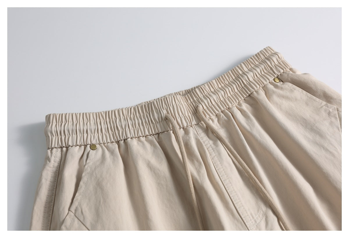 Close-up of beige trousers showing the gathered elastic waistband, drawcords, and pocket openings.