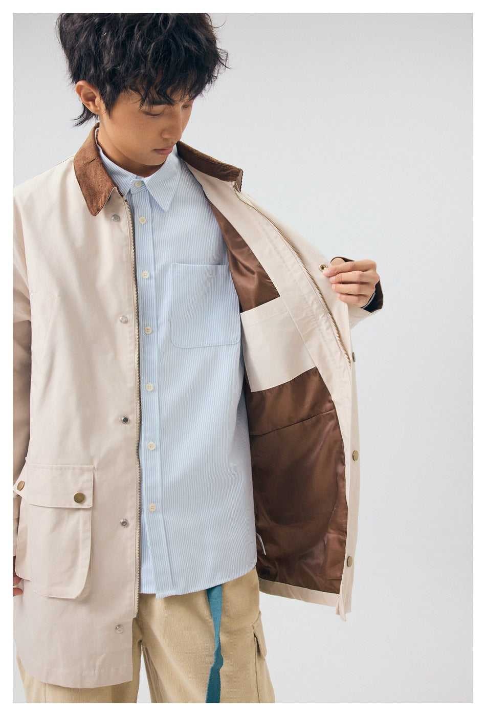 Model opens a light beige coat to show its brown lining, inner pocket, zipper, and brown collar.