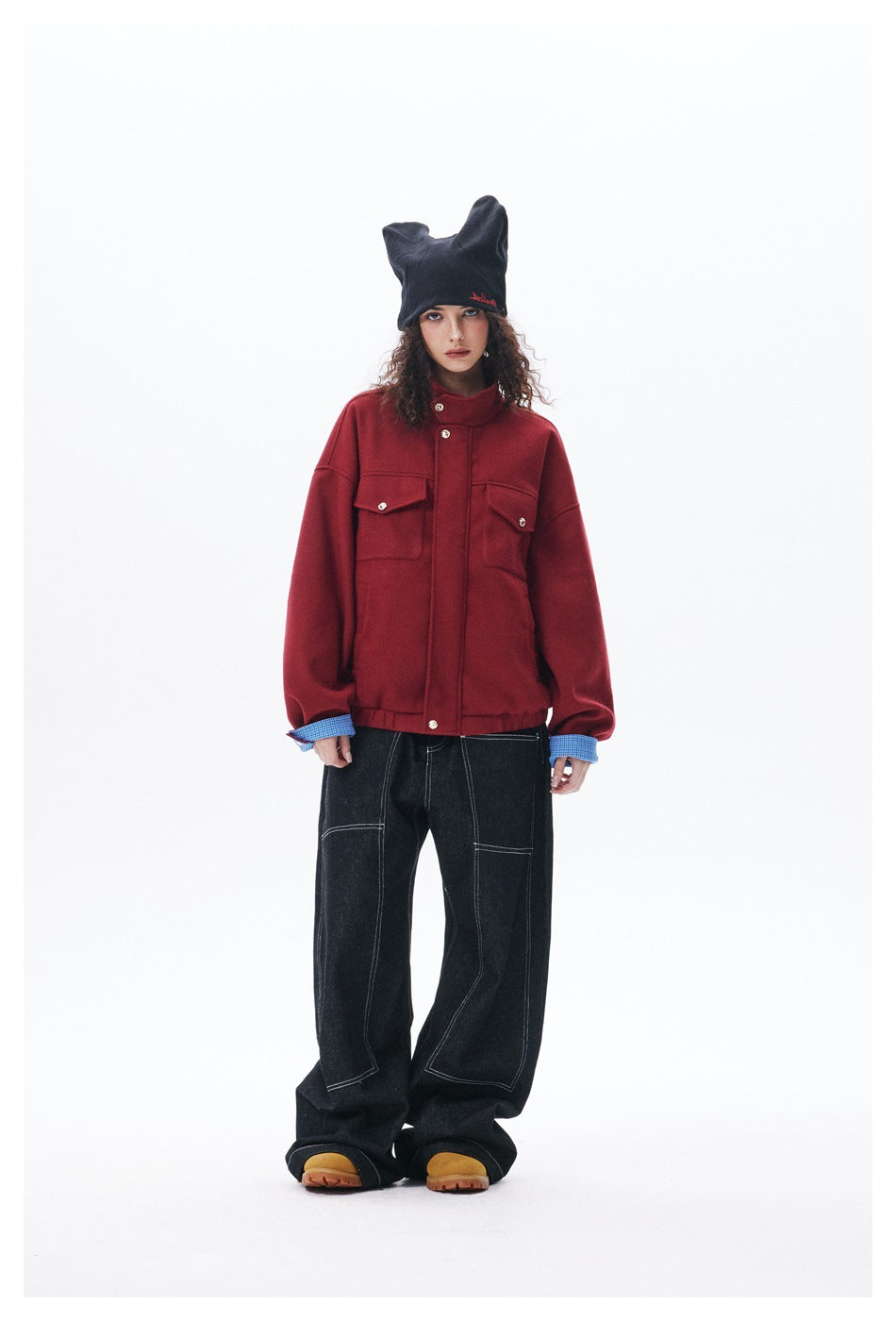Full-length front view of a model in a red button-front jacket with flap pockets, black wide-leg jeans and a black beanie.