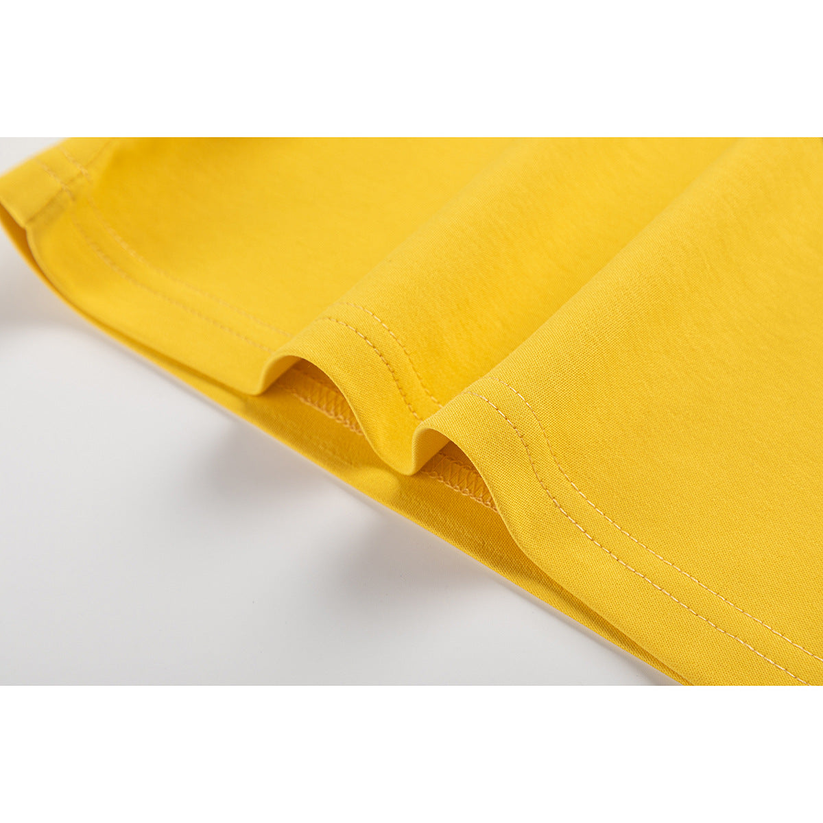 Close-up of the yellow T-shirt's folded hem and parallel rows of stitching.