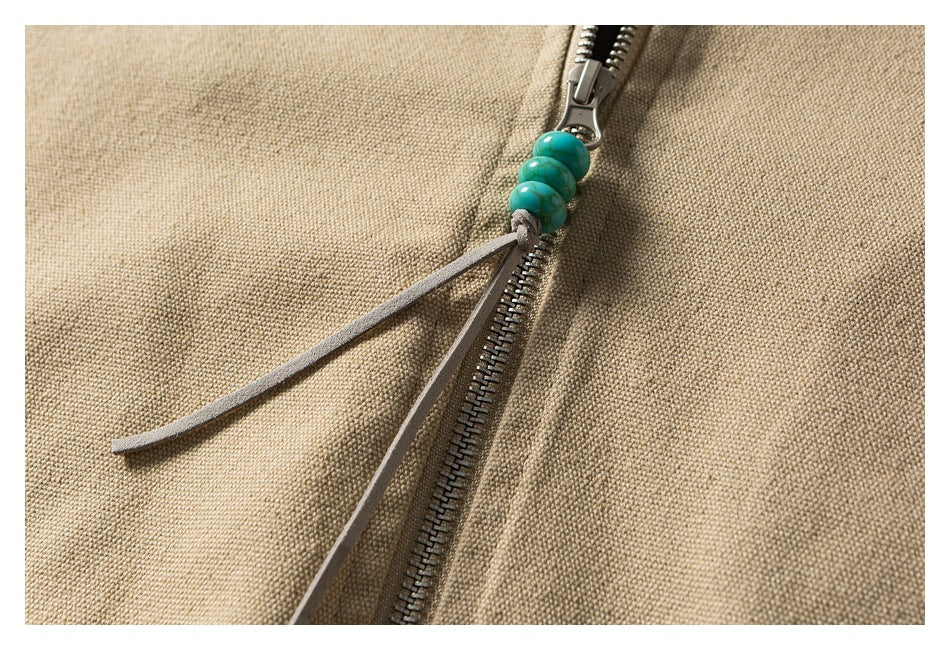 Close-up of a metal zipper pull with turquoise beads and dangling cords on beige fabric.