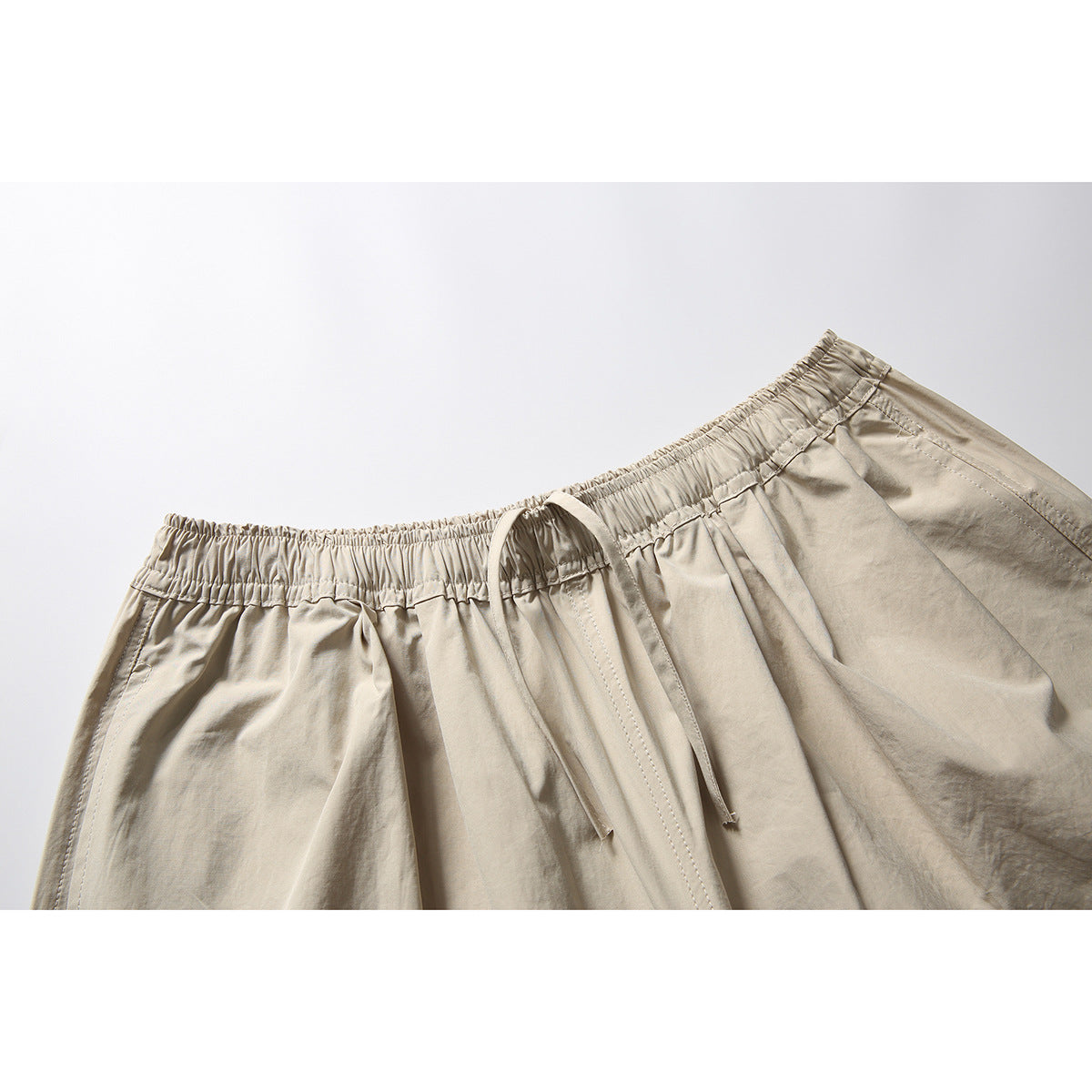 Close-up of light beige pants showing the gathered elastic waistband, drawstrings, and stitching.