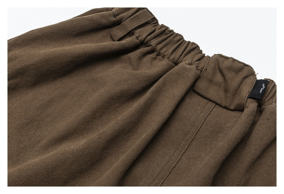Close-up of brown trousers showing the gathered elastic waistband and a small black sewn-in tag.