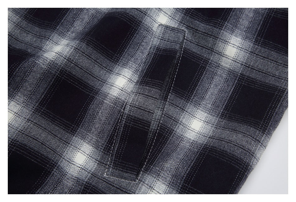 Close-up of a stitched pocket on black, gray, and white plaid fabric.