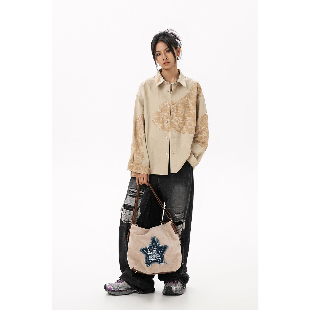Model wearing a beige shirt with tan textured panels and distressed black jeans, holding a logo-print beige tote.