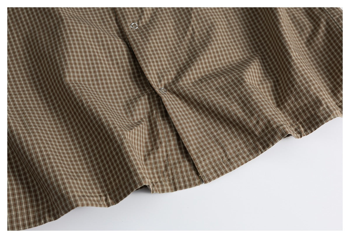 Close-up of the lower front and hem of a brown checked shirt, showing snap fasteners.
