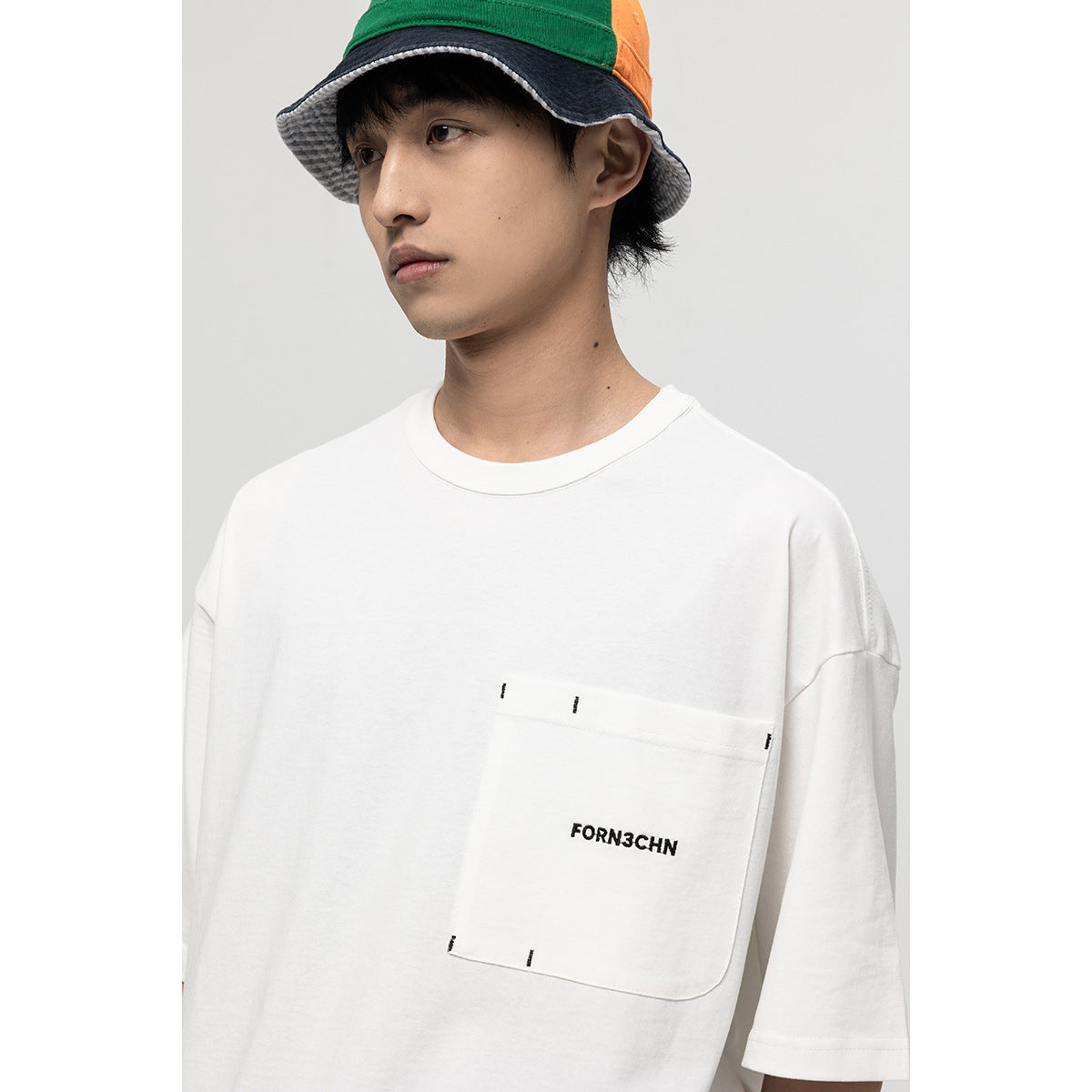 Close view of a white T-shirt's stitched chest pocket with black text and short black stitch accents.