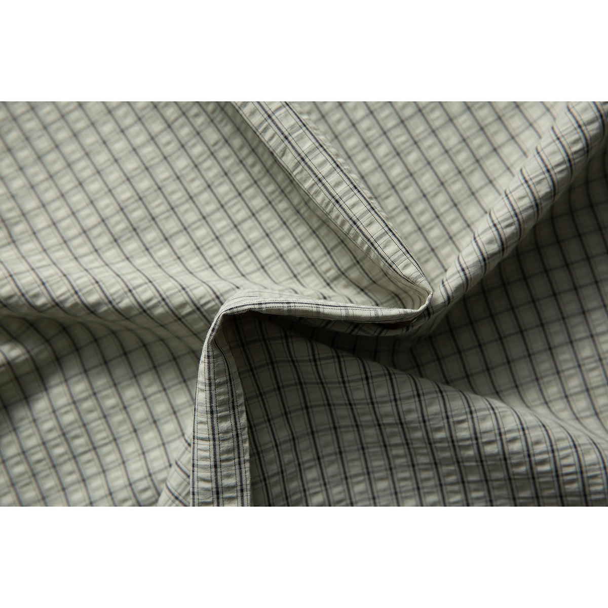 Close-up of pale gray-green plaid shirt fabric draped to show its pattern and stitching.