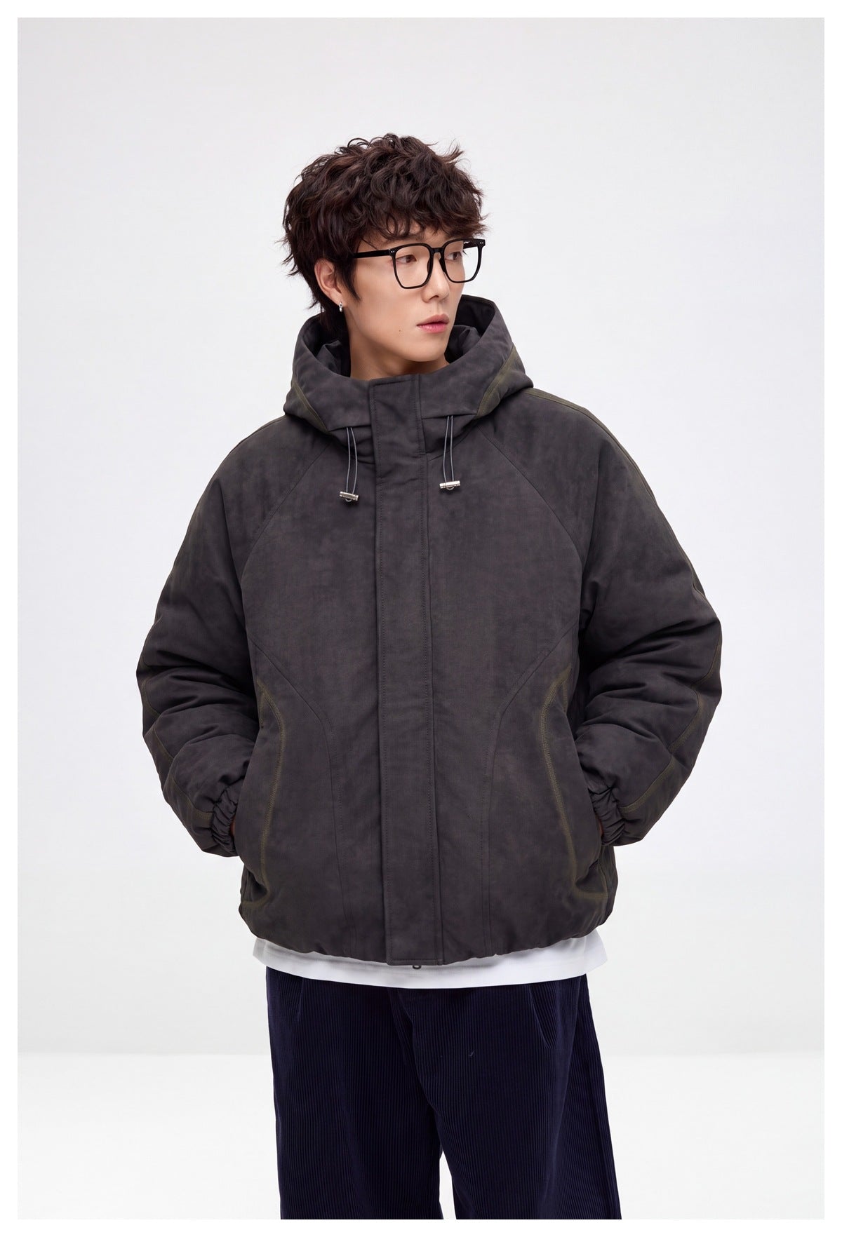 Model wearing a dark gray hooded jacket with hands in pockets, over a white tee and navy corduroy pants