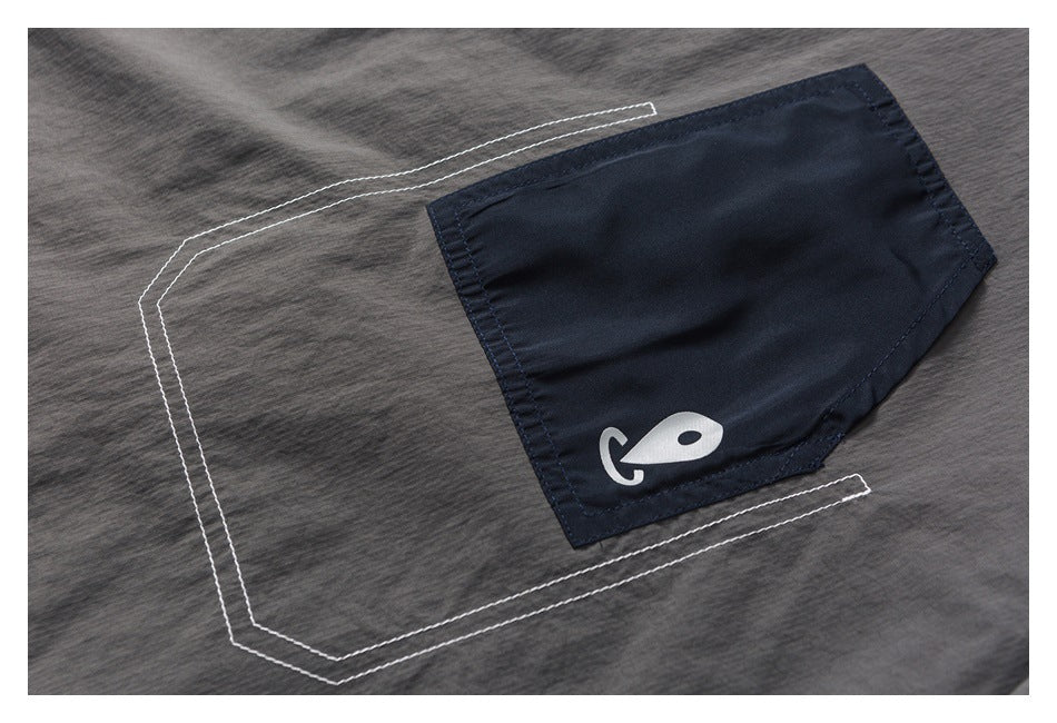 Close-up of a charcoal gray top with a navy pocket, white fish symbol, and contrast stitching.
