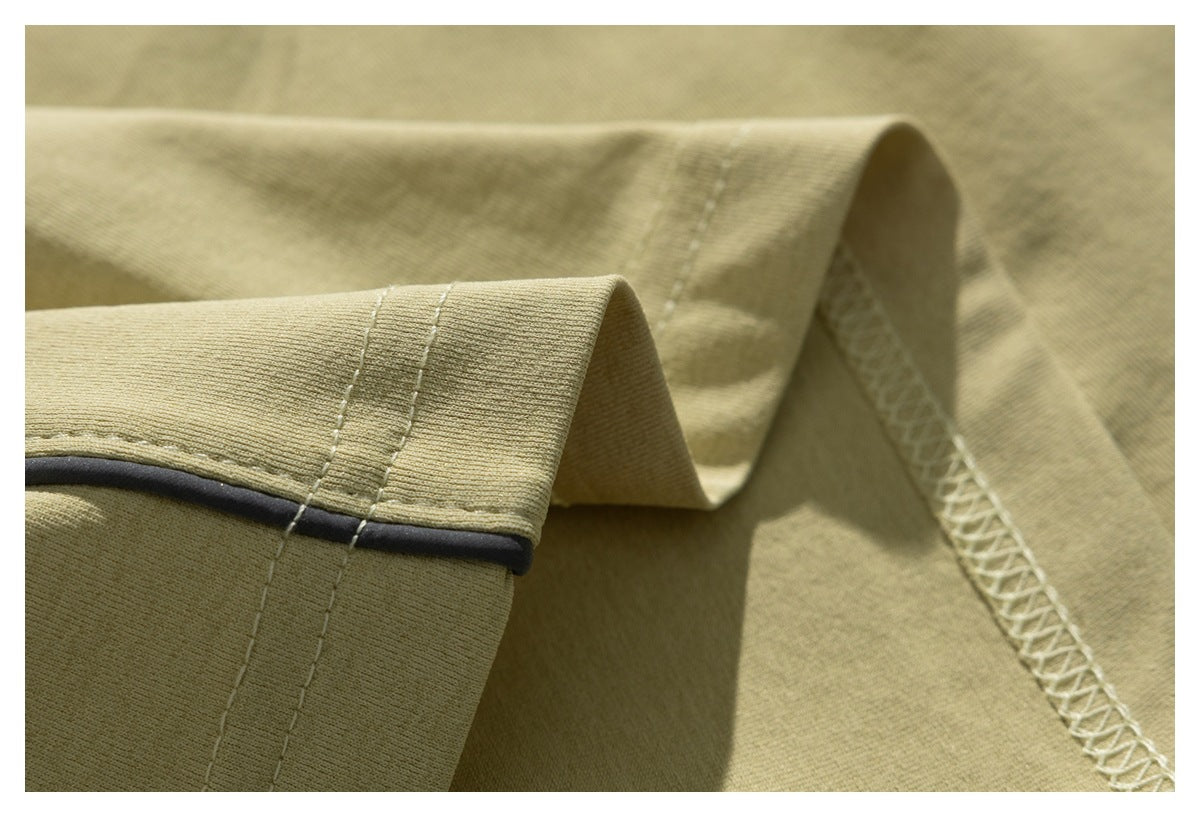 Close-up showing the pale olive T-shirt's ribbed sleeve edge, dark piping, and interior overlock stitching.