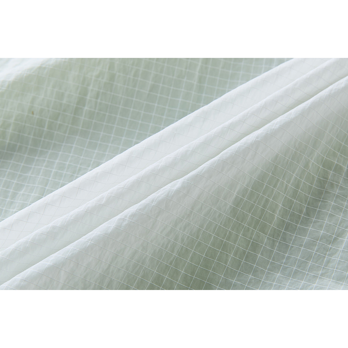 Close-up of the pale green fabric's fine white grid pattern and layered edges.