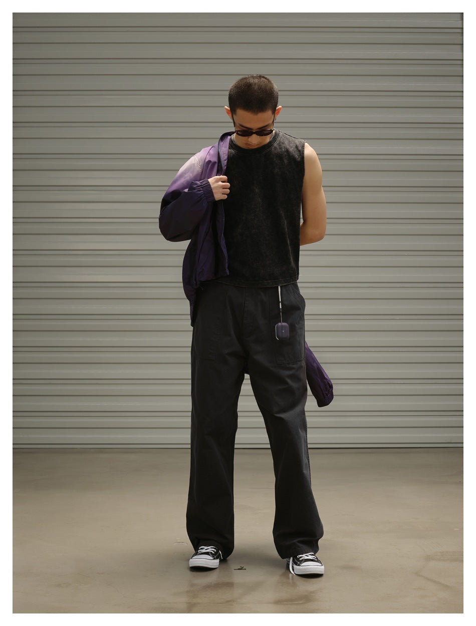 Model wearing a black sleeveless top and loose black trousers, with a purple jacket draped over one shoulder.