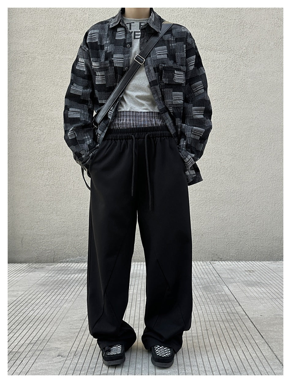 Person wearing black wide-leg drawstring pants with a patterned dark shirt, gray top and crossbody bag, full-length view