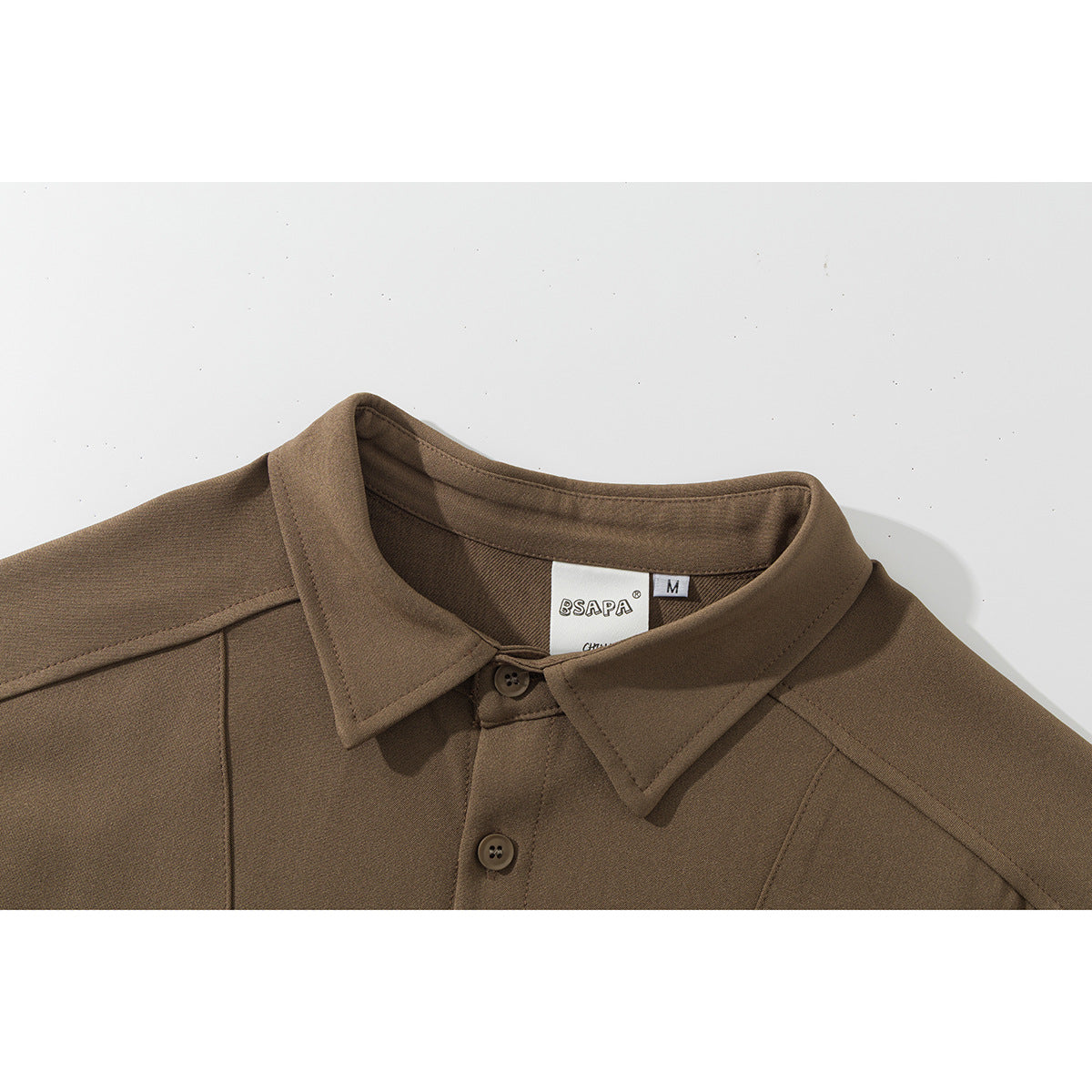 Close-up of a brown shirt's pointed collar, shoulder seams, front buttons, and inner size label.