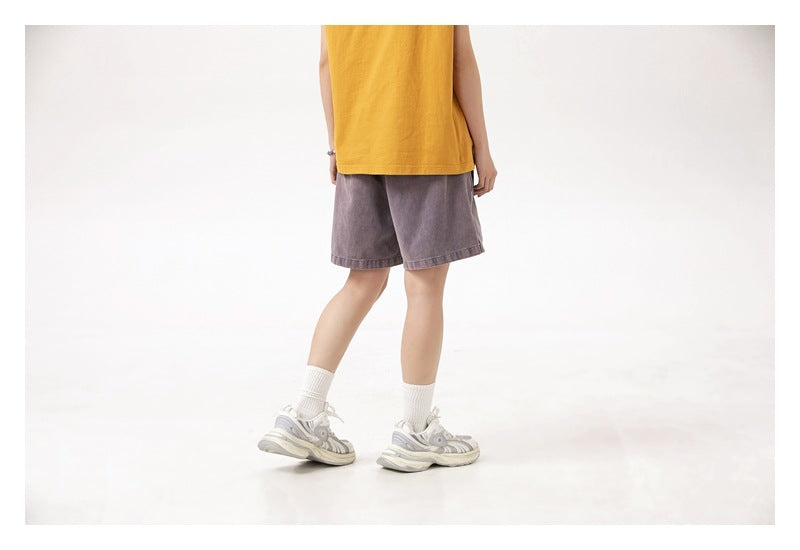 Rear three-quarter view of a model wearing muted purple-gray shorts with a mustard yellow top and white socks.