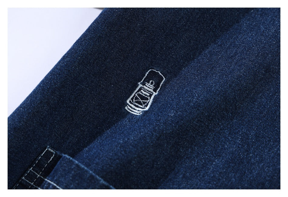 Close-up of a small white embroidered bottle-shaped motif on dark indigo denim.
