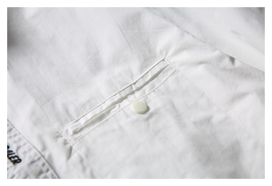 Close-up of a narrow buttoned pocket detail on the white shirt.