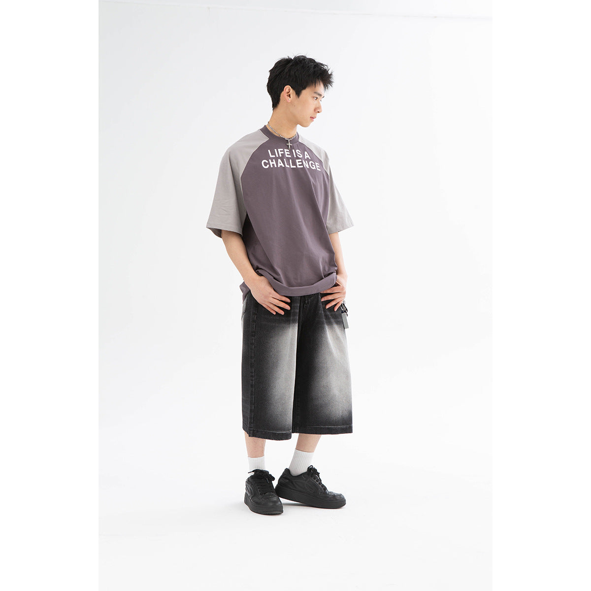 Model wearing a charcoal raglan T-shirt with gray sleeves and white “LIFE IS A CHALLENGE” text, plus black shorts.