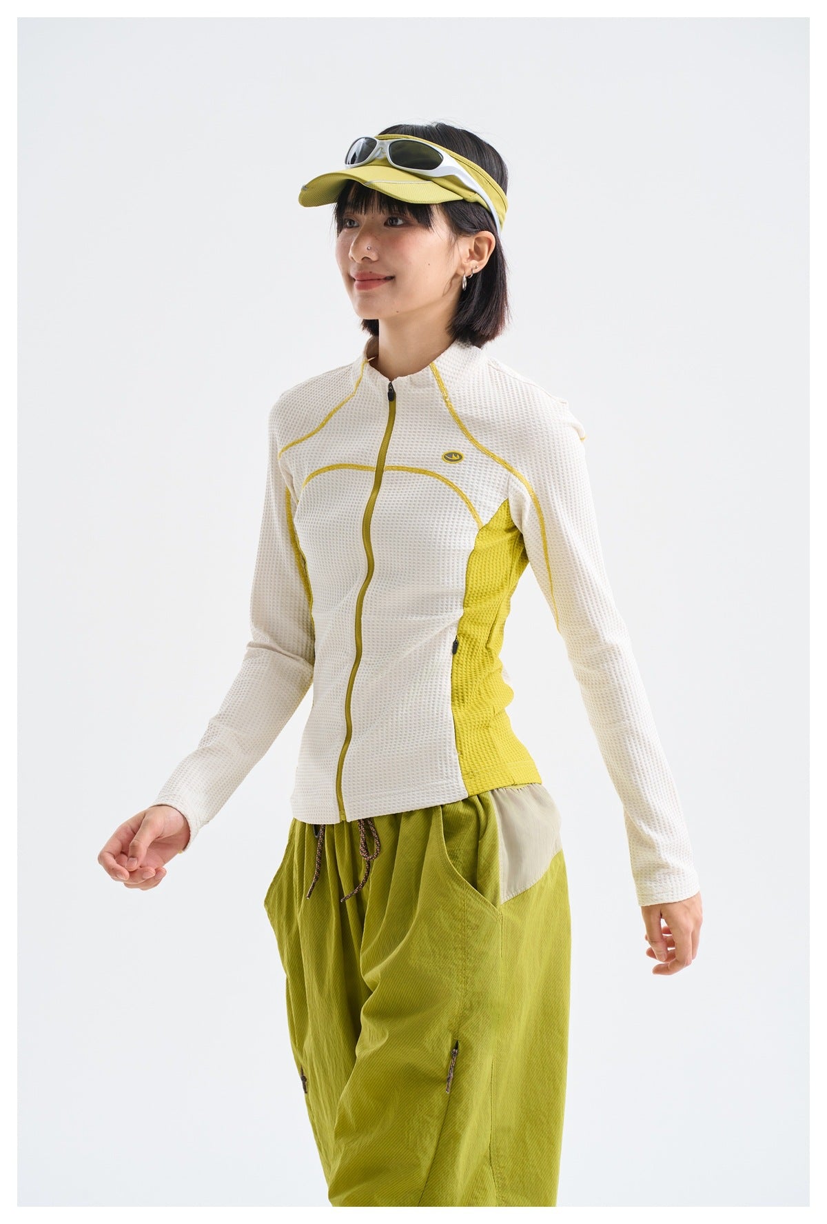 Three-quarter view of a model wearing a white textured jacket with yellow accents and olive-green pants.