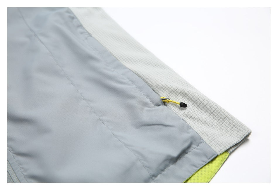 Close-up of a gray jacket edge with a yellow zipper pull, pale grid-textured lining, and a glimpse of neon yellow fabric.