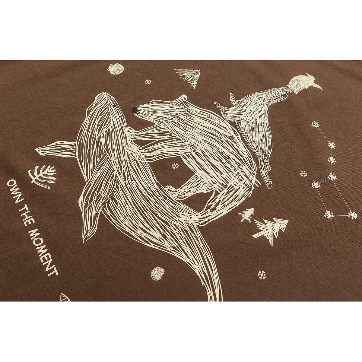 Close-up of cream animal and star illustrations with the words “OWN THE MOMENT” printed on brown fabric.