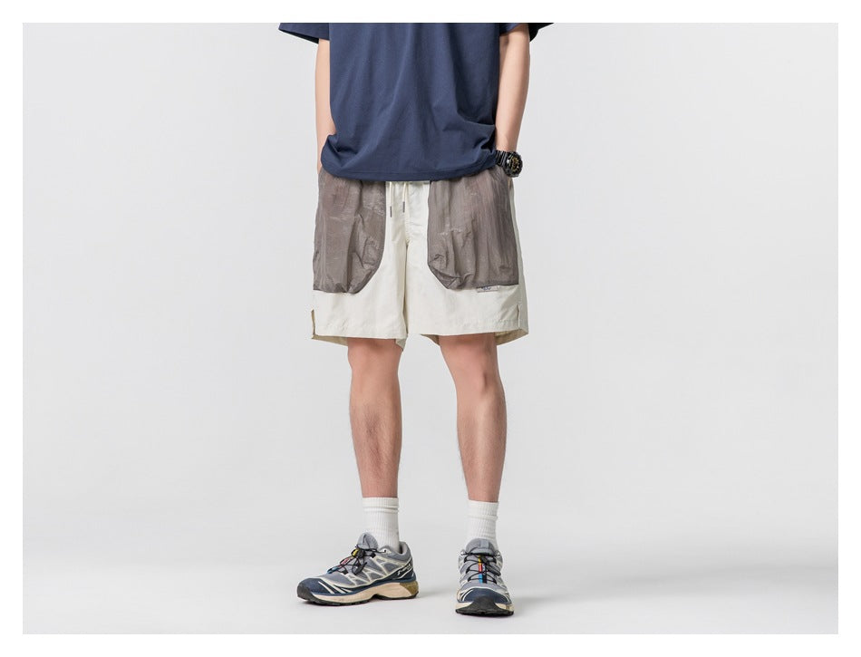 Cropped model wearing cream shorts with large gray patch pockets and a navy T-shirt, front view.