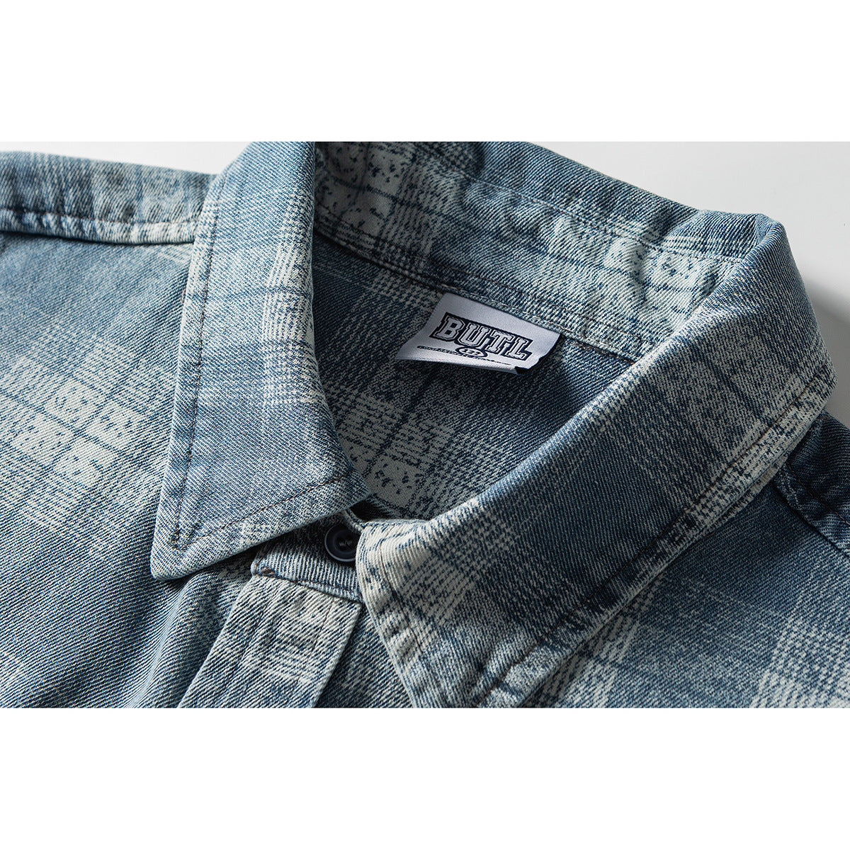 Close-up of a blue and gray patterned denim shirt collar with a visible sewn-in neck label and dark button.