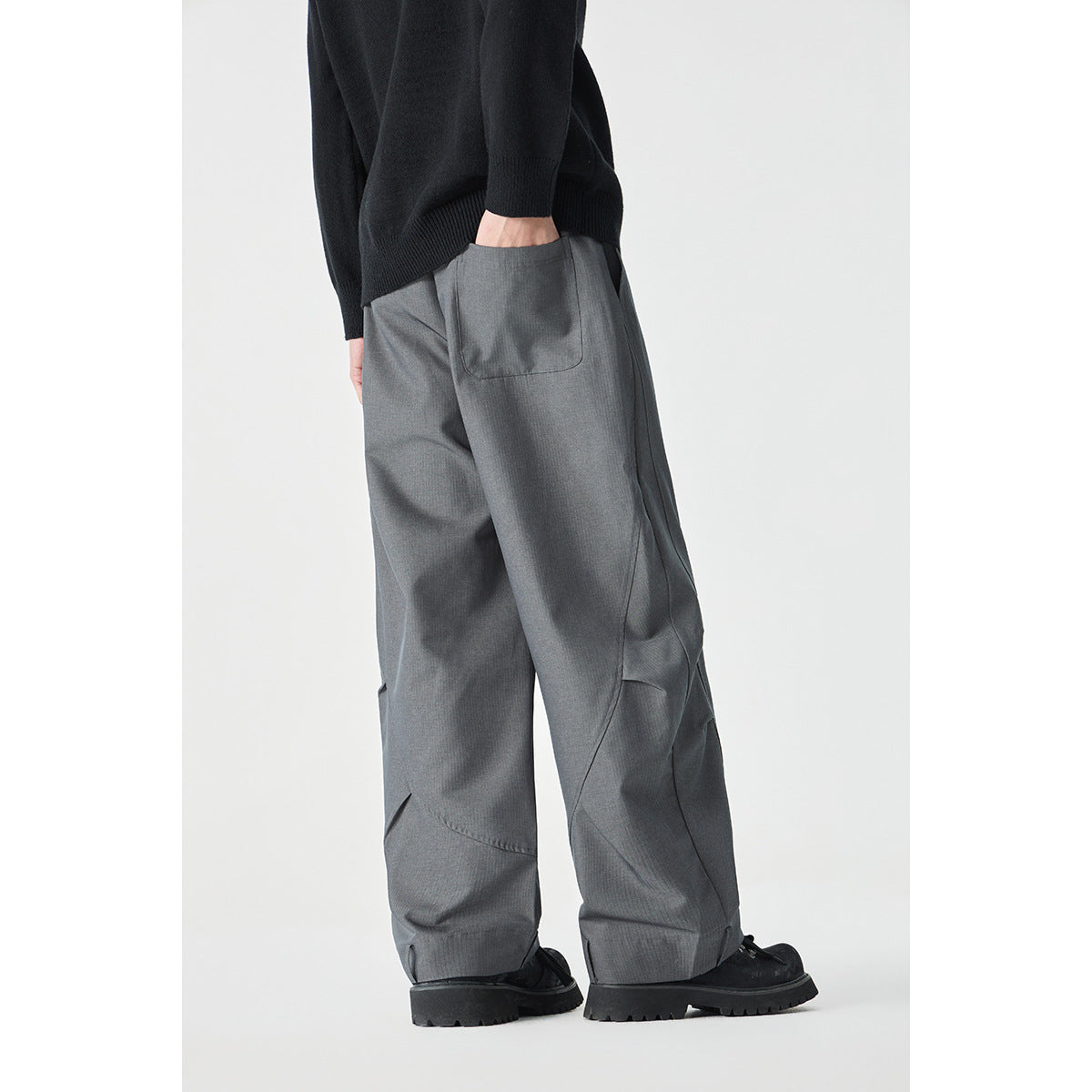 Model wearing loose gray pants, showing the rear pocket and curved leg seams from a back-side angle.