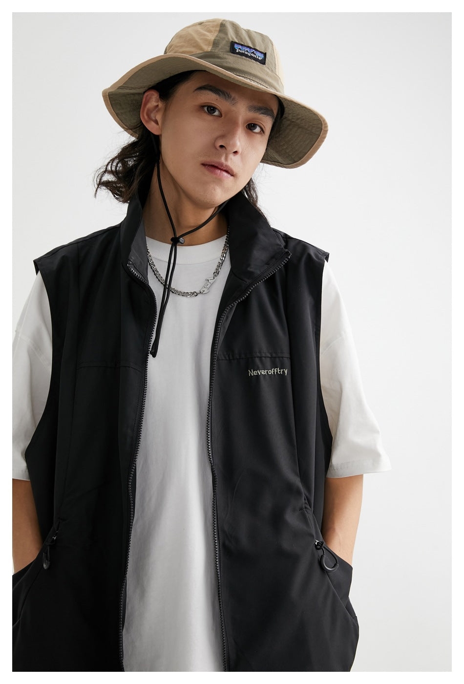 Close view of a model wearing a black sleeveless zip vest with a high collar and drawcord pockets.