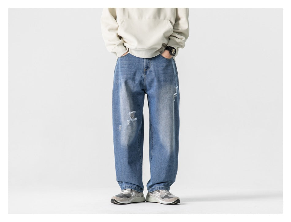 Person wearing blue washed wide-leg ripped jeans with a cream hoodie and gray sneakers, hands in pockets, front view